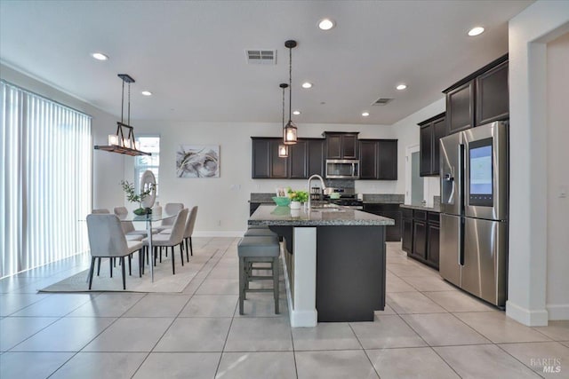 kitchen with dark brown cabinetry, sink, hanging light fixtures, a center island with sink, and appliances with stainless steel finishes