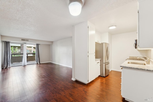 kitchen featuring dark hardwood / wood-style floors, stainless steel refrigerator, sink, white cabinets, and a textured ceiling