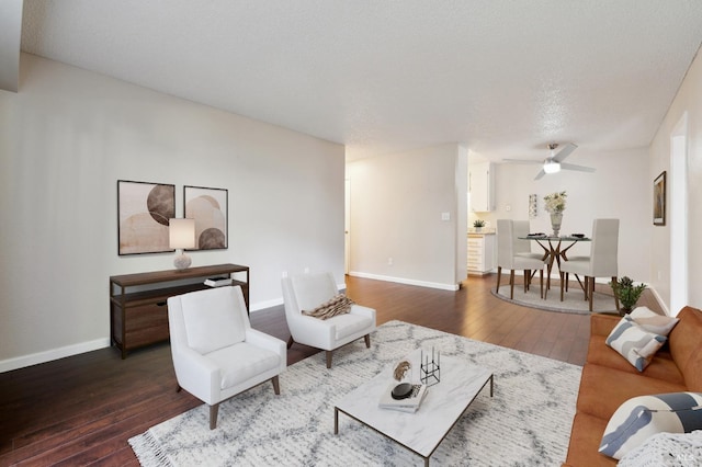 living room with a textured ceiling, dark wood-type flooring, and ceiling fan