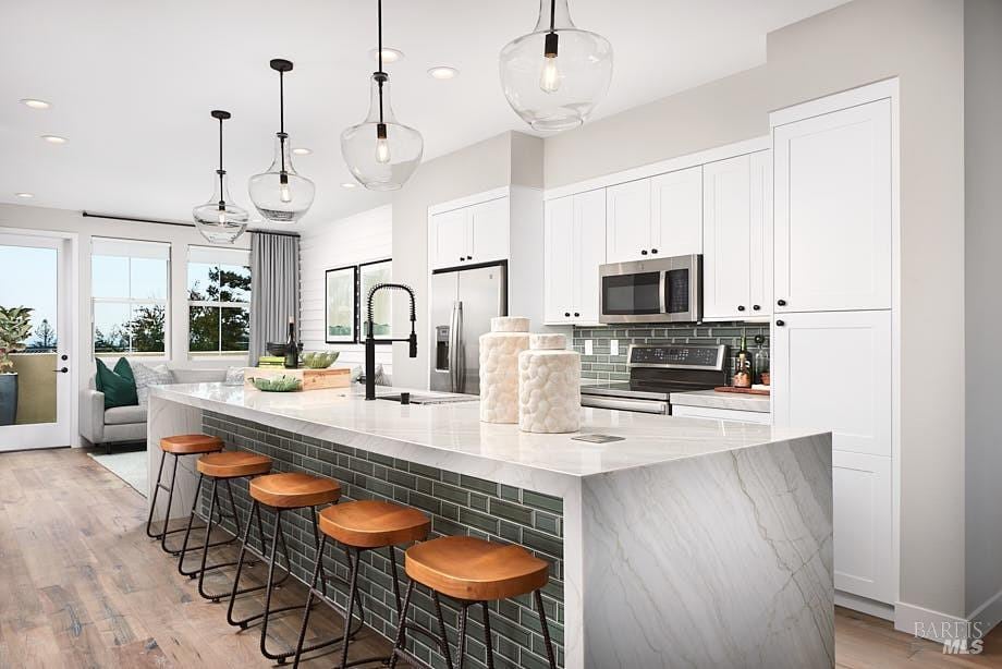 kitchen with appliances with stainless steel finishes, decorative light fixtures, a kitchen bar, and a spacious island