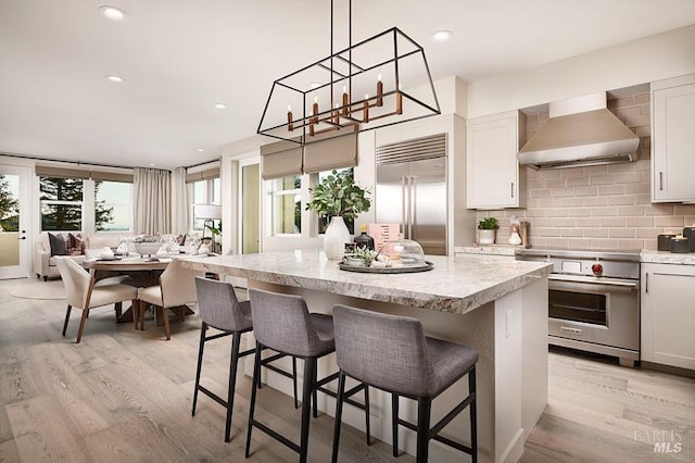 kitchen featuring a kitchen island, white cabinetry, premium appliances, light hardwood / wood-style floors, and wall chimney exhaust hood