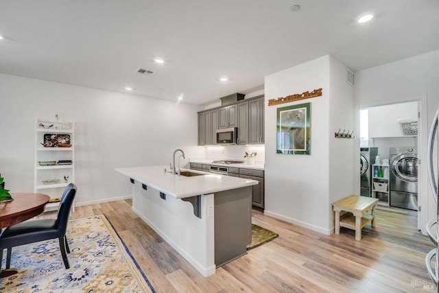 kitchen featuring a breakfast bar area, a center island with sink, washer and dryer, appliances with stainless steel finishes, and gray cabinets