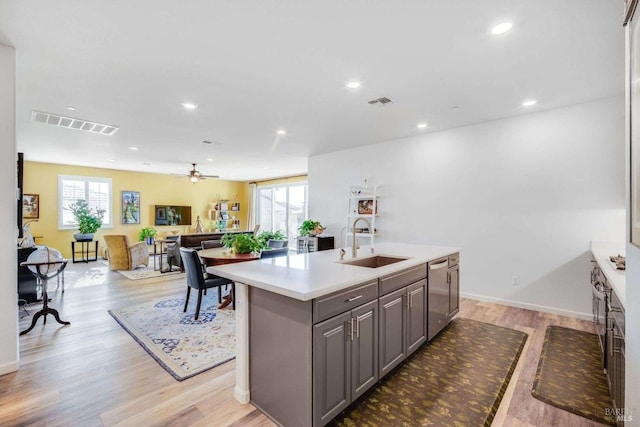 kitchen with gray cabinets, an island with sink, sink, ceiling fan, and light hardwood / wood-style floors