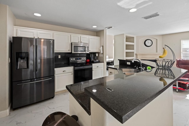 kitchen with sink, an island with sink, stainless steel appliances, decorative backsplash, and white cabinets