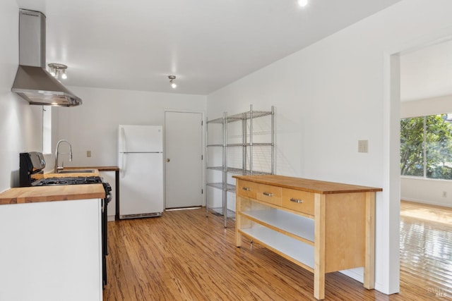 kitchen with sink, wooden counters, white refrigerator, light hardwood / wood-style floors, and island exhaust hood