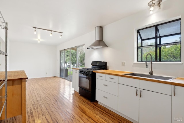 kitchen featuring sink, black range with gas stovetop, white cabinets, and wall chimney exhaust hood