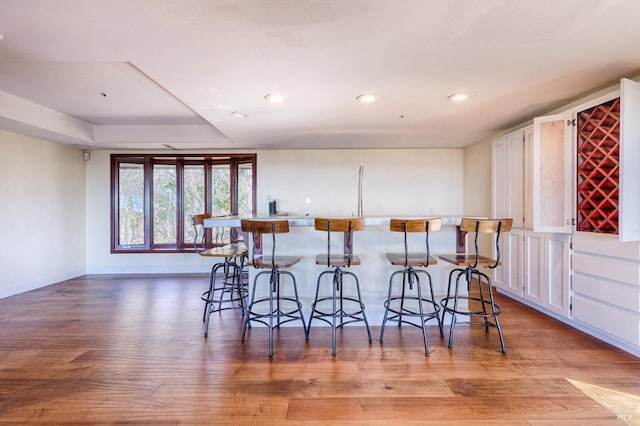 kitchen with a tray ceiling, light wood-type flooring, white cabinetry, and a kitchen bar