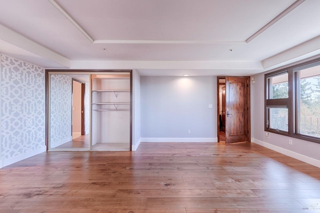 unfurnished bedroom featuring light wood-type flooring, a raised ceiling, and a closet