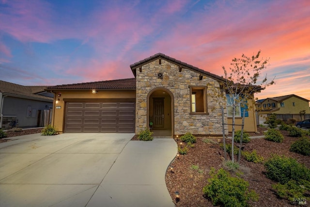 view of front facade featuring stucco siding, a tiled roof, driveway, stone siding, and an attached garage