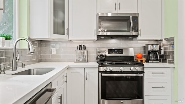 kitchen with a sink, white cabinetry, appliances with stainless steel finishes, decorative backsplash, and glass insert cabinets