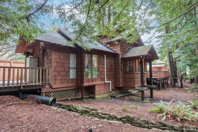 view of side of home featuring a wooden deck, roof with shingles, and fence