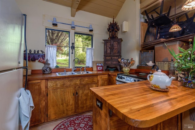 kitchen with a sink, lofted ceiling with beams, freestanding refrigerator, brown cabinetry, and wooden counters