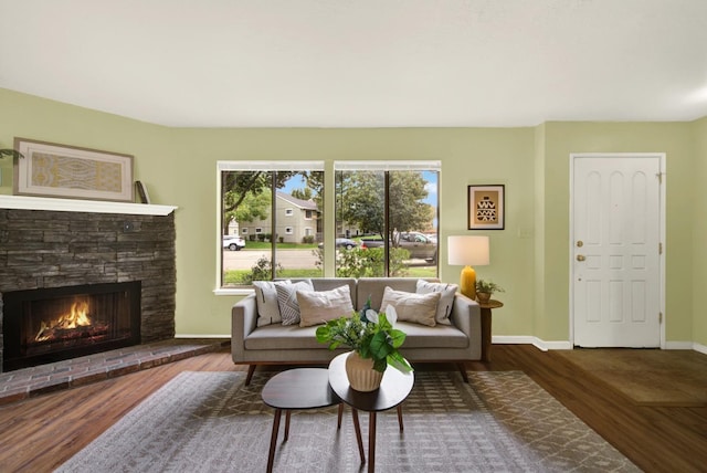 living room featuring dark wood-type flooring, a stone fireplace, and a wealth of natural light