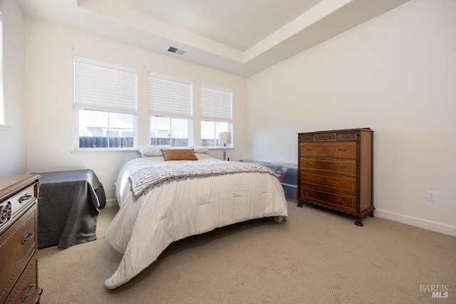 bedroom with light carpet, a tray ceiling, visible vents, and baseboards