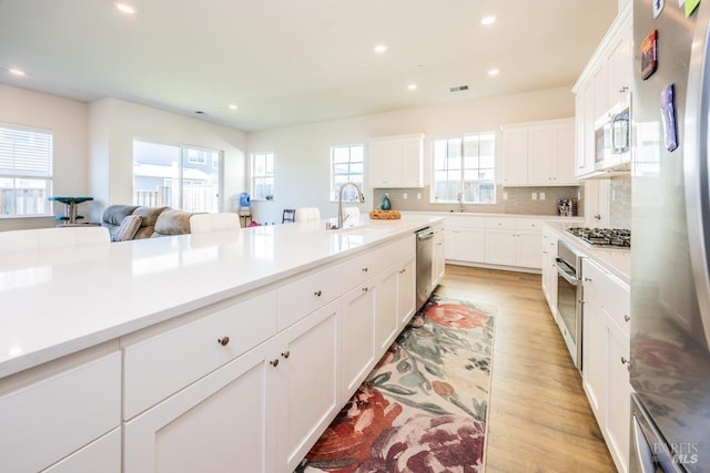 kitchen with light wood finished floors, stainless steel appliances, light countertops, white cabinetry, and a sink