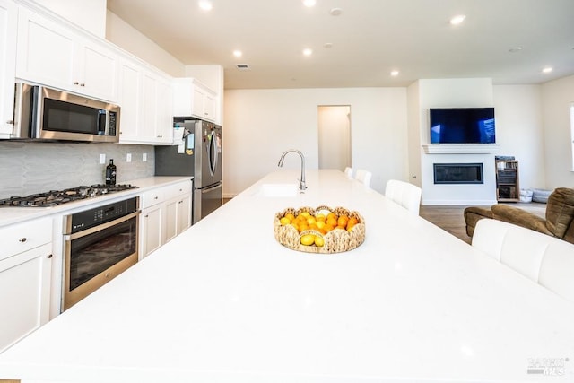 kitchen featuring stainless steel appliances, light countertops, a glass covered fireplace, white cabinets, and a sink