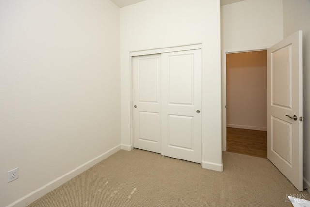 unfurnished bedroom with light carpet, a closet, and baseboards