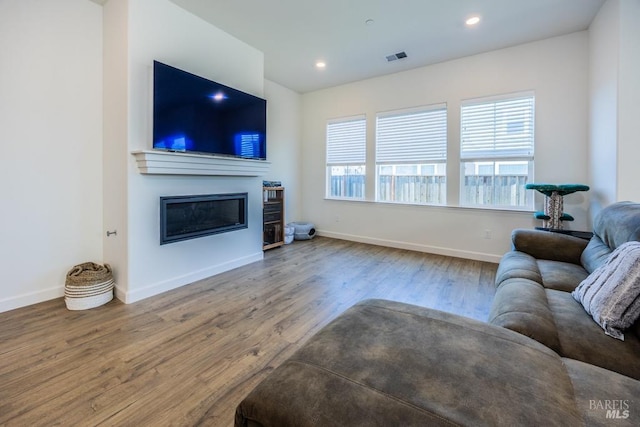 living area with recessed lighting, visible vents, a glass covered fireplace, wood finished floors, and baseboards