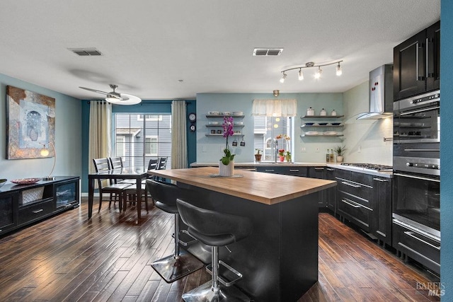 kitchen with a kitchen island, a breakfast bar, dark hardwood / wood-style floors, ventilation hood, and stainless steel gas stovetop