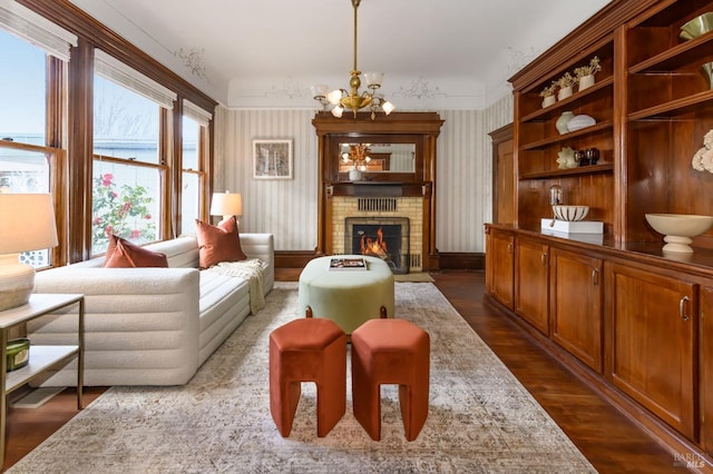living area with a chandelier, dark wood-type flooring, a brick fireplace, wallpapered walls, and baseboards