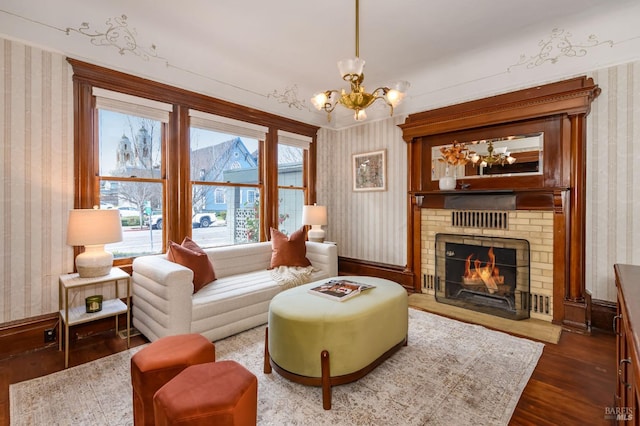 sitting room featuring wallpapered walls, a chandelier, dark wood-style floors, a brick fireplace, and baseboards