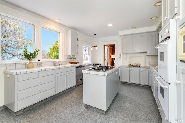 kitchen featuring appliances with stainless steel finishes, tile countertops, a sink, a center island, and decorative light fixtures