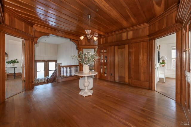 empty room with a chandelier, wood finished floors, wooden walls, plenty of natural light, and wood ceiling