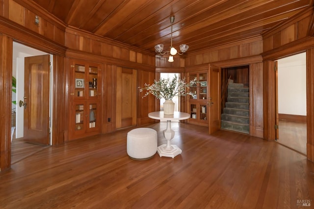 unfurnished dining area featuring wood ceiling, a chandelier, wooden walls, stairway, and wood finished floors