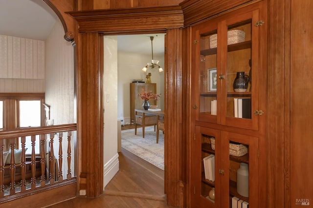 hallway featuring baseboards, wood finished floors, and arched walkways