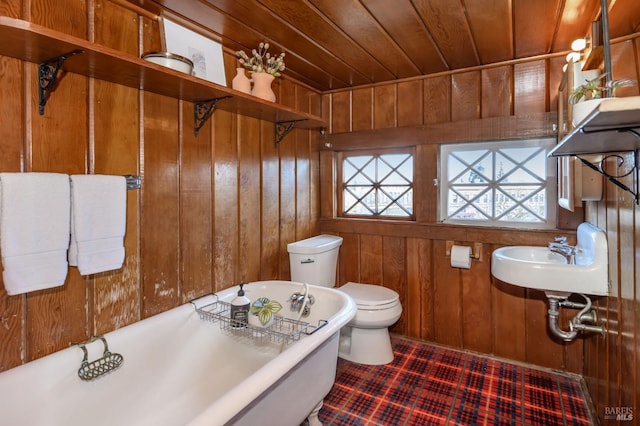 bathroom with wood walls, toilet, wooden ceiling, a freestanding tub, and a sink