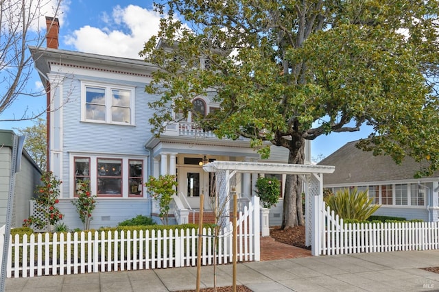 italianate house featuring a chimney and a fenced front yard