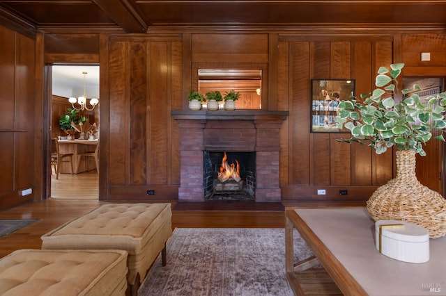 living area with wooden walls, a brick fireplace, wood finished floors, beamed ceiling, and a chandelier