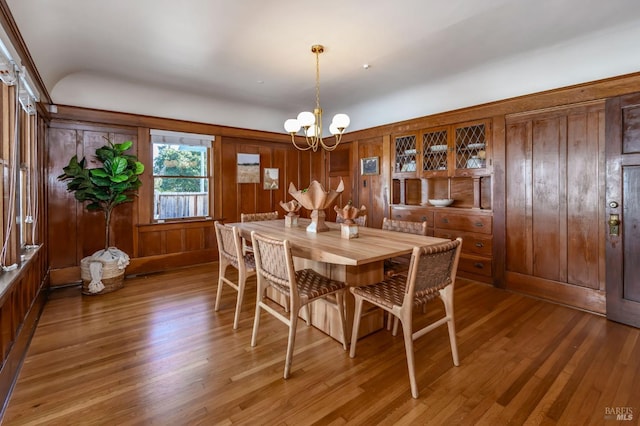 dining space with a chandelier, wood finished floors, and wood walls
