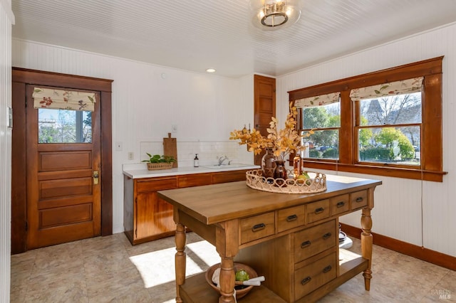 kitchen featuring healthy amount of natural light, baseboards, brown cabinets, wooden walls, and a sink