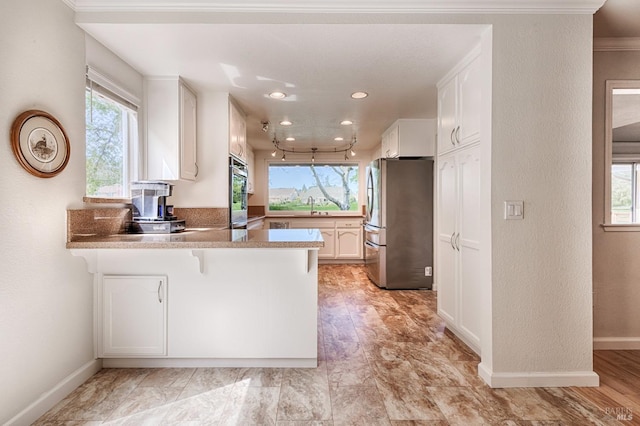 kitchen with a sink, appliances with stainless steel finishes, a peninsula, white cabinets, and a healthy amount of sunlight
