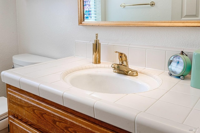 bathroom with a textured wall, toilet, and vanity