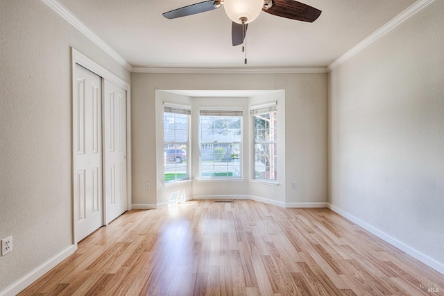 spare room featuring crown molding, light wood-type flooring, a textured wall, baseboards, and ceiling fan