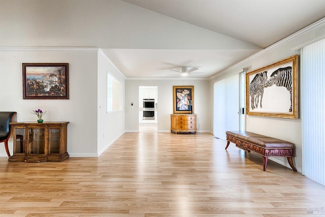 interior space featuring vaulted ceiling, ornamental molding, baseboards, ceiling fan, and light wood-style flooring