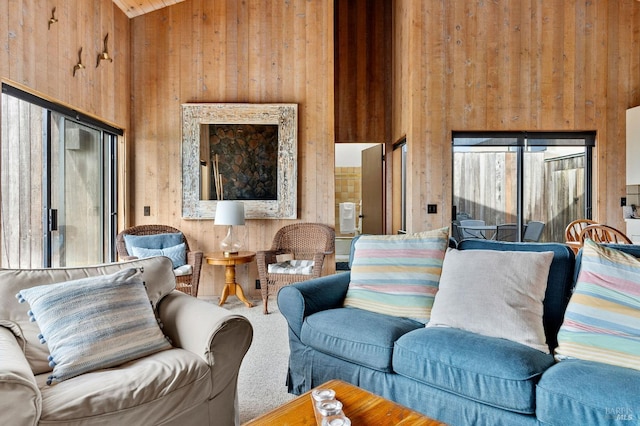 carpeted living room with plenty of natural light, high vaulted ceiling, and wood walls