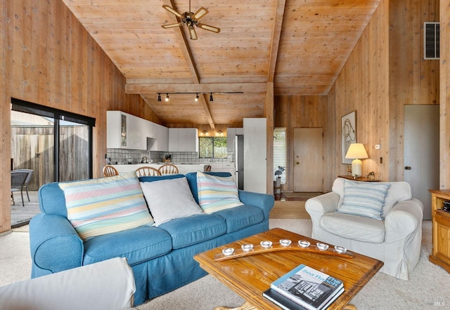 carpeted living room with ceiling fan, beam ceiling, track lighting, wooden ceiling, and wood walls