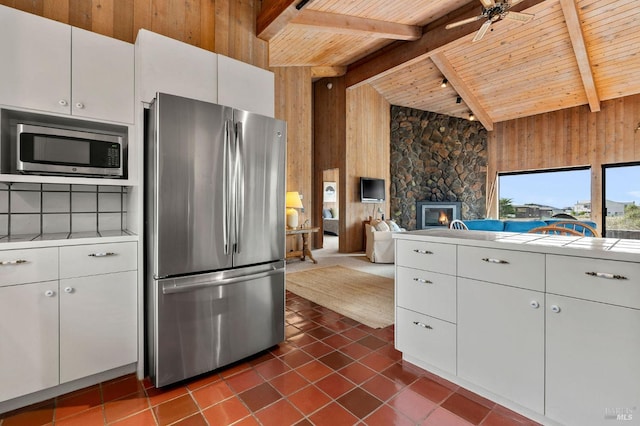 kitchen with wood walls, wood ceiling, appliances with stainless steel finishes, a fireplace, and white cabinets