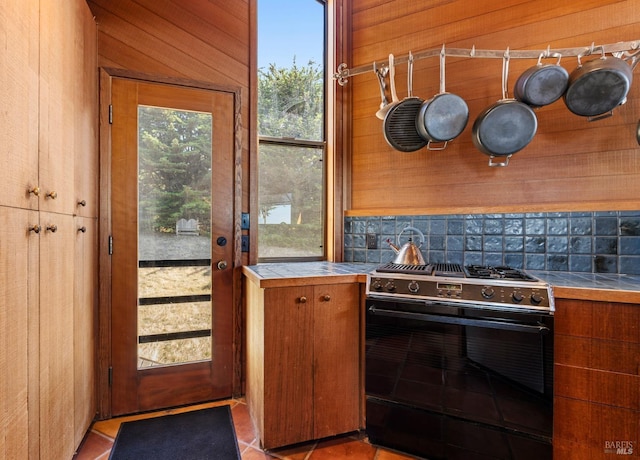 kitchen with wood walls, tile countertops, decorative backsplash, and stainless steel gas range oven