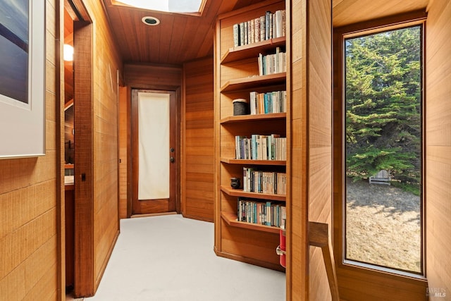 hall featuring carpet floors, a skylight, wood ceiling, and wooden walls