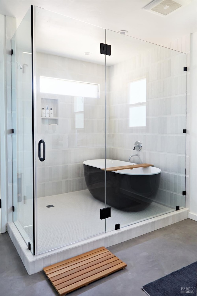 bathroom with finished concrete flooring, a freestanding tub, a shower stall, and visible vents