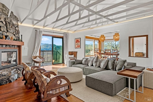 living area featuring beamed ceiling, wood finished floors, a stone fireplace, high vaulted ceiling, and a mountain view