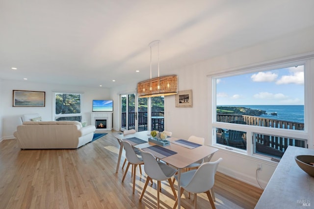 dining space with light wood-type flooring, recessed lighting, baseboards, and a glass covered fireplace