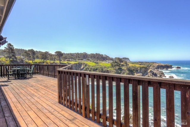 wooden terrace featuring a view of the beach, outdoor dining area, and a water view