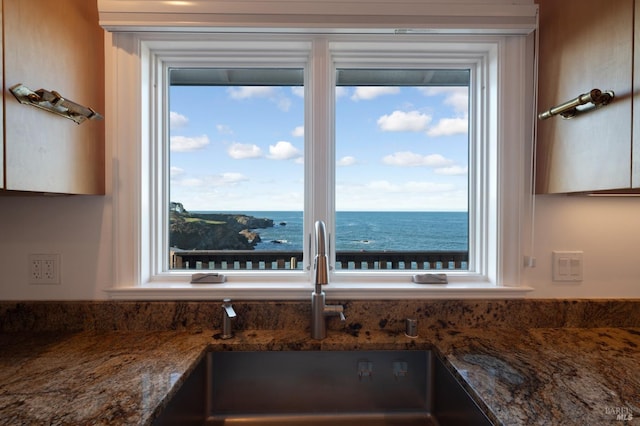 details featuring dark stone counters, a water view, and a sink