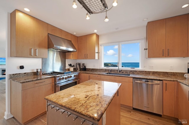 kitchen featuring wall chimney exhaust hood, appliances with stainless steel finishes, a center island, a water view, and a sink