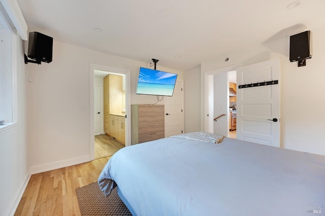 bedroom featuring baseboards, ensuite bathroom, and light wood-style floors